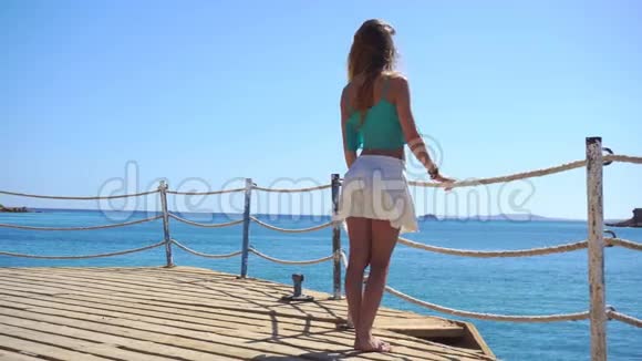 一个留着长发和白裙子的女孩站在码头上看着大海视频的预览图