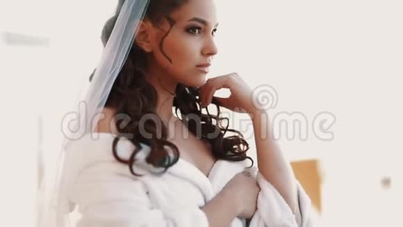 年轻的新娘穿着白色长袍站在阳台上等待未婚夫视频的预览图
