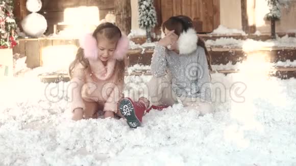 圣诞节或新年穿着毛皮耳机的孩子坐在人造雪上两个小女孩的肖像姐妹姐妹姐妹视频的预览图