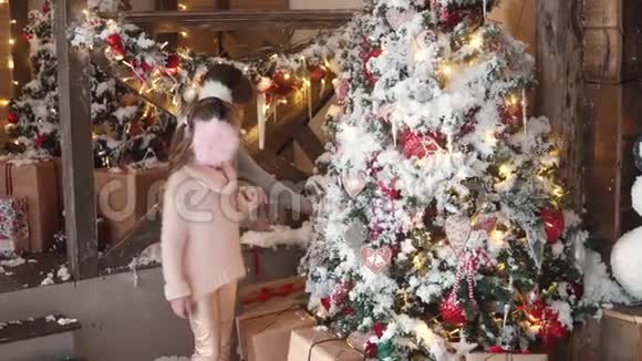 圣诞节或新年孩子们迷人地看着新年树有毛的小女孩把圣诞玩具挂在耳朵上视频的预览图