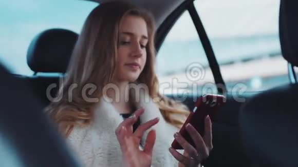一位漂亮的年轻女士她的蓝眼睛和一头金发在开车进来的时候用手机应用程序给她的朋友发信息视频的预览图