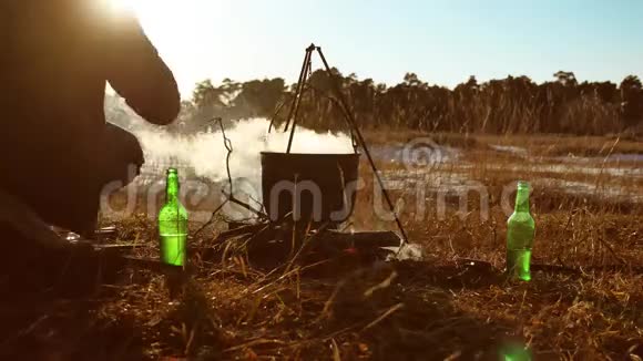 一个人点燃篝火徒步旅行者停在露营地徒步旅行者水壶里的水沸腾在日落时点燃阳光视频的预览图