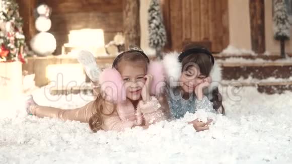 圣诞节或新年两个穿着毛皮耳机的小妹妹的肖像孩子们躺在人造雪上视频的预览图