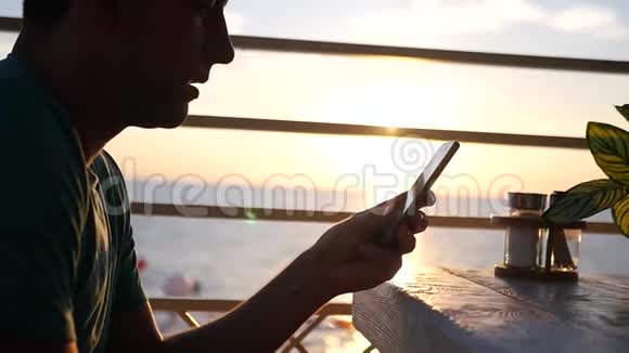 日落时分一个带电话的年轻人在咖啡馆里高清1920x1080慢动作视频的预览图