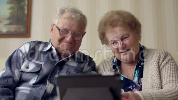 高级夫妻在沙发上使用电子标签一对快乐的老夫妇在数码平板电脑上视频聊天视频的预览图