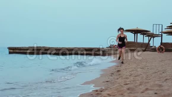 那个运动女孩沿着海浪翻滚的沙滩奔跑布鲁内特早上在海岸线上慢跑视频的预览图