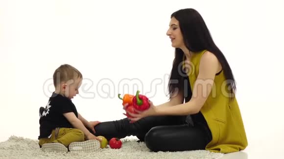 妈妈和孩子坐在地板上周围有很多蔬菜和水果白色背景慢动作视频的预览图