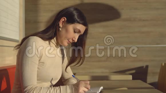 年轻的黑发女人坐在咖啡馆里在笔记本上做笔记视频的预览图