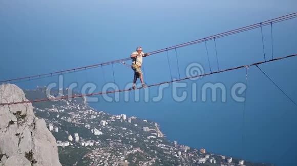 一个人在岩石海洋和城市的背景下在高空的悬索桥上行走高清1920x1080视频的预览图