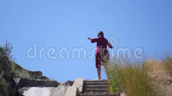 女孩在旋转站在楼梯的顶端在一股风中逆着天空和草地3840x21604K视频的预览图