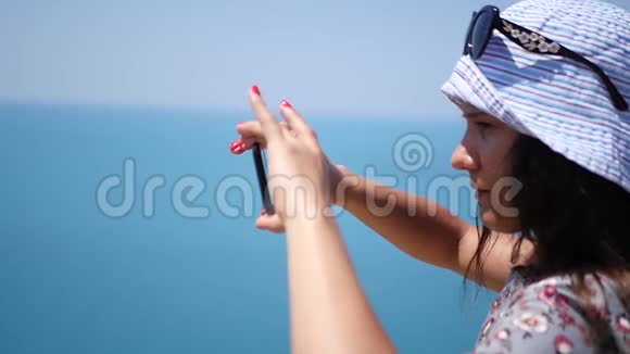 戴着帽子的漂亮年轻女孩在电话里拍摄了大海的全景高清1920x1080慢动作视频的预览图