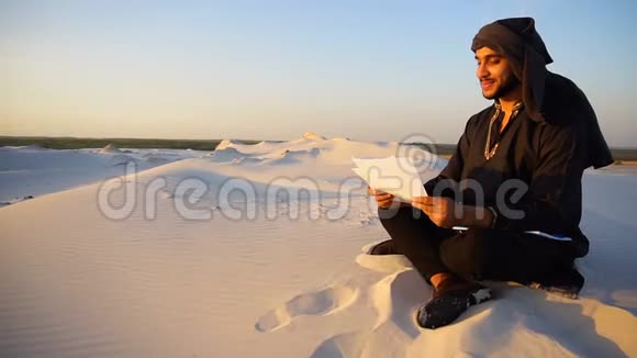 成功的阿联酋商人读商业计划书夏天晚上坐在沙漠中的温暖的沙滩上视频的预览图