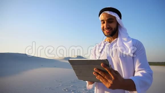 夏天在大沙漠中站着的一幅欢快的阿拉伯游客画像他在小工具上打印笔记视频的预览图