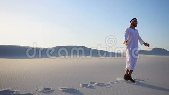 快乐的男性阿拉伯谢赫走在白沙沙漠在新的一天和晴朗的夏天视频的预览图