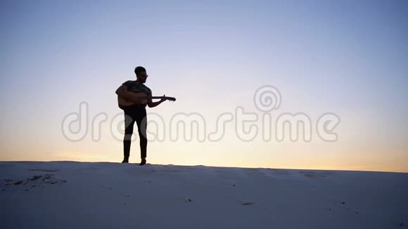 肌肉发达的年轻男性穆斯林正在练习吉他演奏晚上在日落时站在沙漠山上露天表演视频的预览图