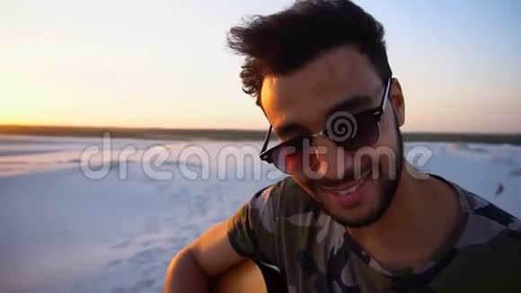 夏季日落时分在一望无际的沙漠中弹吉他的阿拉伯人的特写肖像画视频的预览图