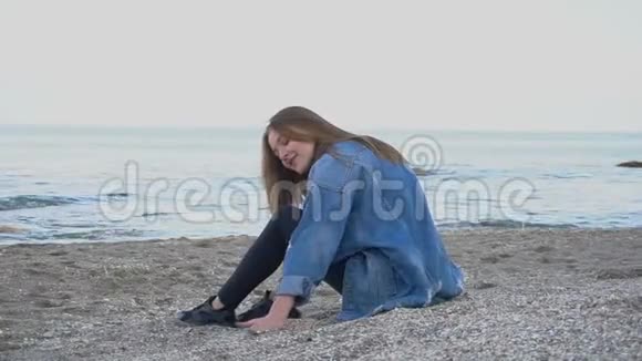 独自一个微笑的年轻女人坐在海边放松在沙滩上欣赏大自然下午带着贝壳视频的预览图
