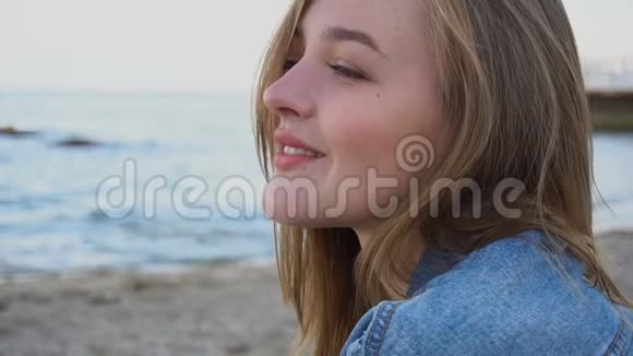 慢镜头拍摄的快乐女孩的肖像她在镜头前摆姿势可爱的笑声坐在蓝色的大海和沙滩上视频的预览图