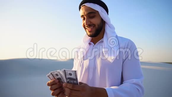 成功的阿拉伯酋长认为钞票和快乐站在沙漠中心温暖的夏日视频的预览图