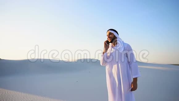 在炎热的夏天穆斯林男性商人和同伴在沙漠中站着通过电话交谈并分享消息视频的预览图