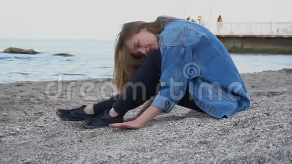 微笑的年轻女子在海滩上休息并在镜头中摆姿势坐在沙滩上在温暖的春天夜晚贝壳视频的预览图