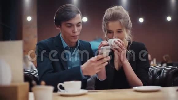 一对年轻夫妇在咖啡馆约会一个手里拿着智能手机的男人和一个正在喝咖啡的女孩很活泼视频的预览图