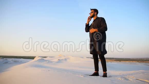 英俊的阿拉伯男性商人谈论蜂窝商业专业站在沙沙沙漠中露天夏季视频的预览图