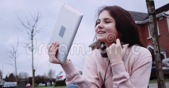 穿着粉红色背心的漂亮女孩在乡间大街前拿着平板电脑年轻女孩使用平板电脑面带微笑视频的预览图