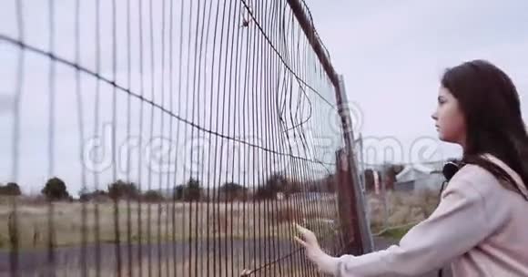 金属栅栏附近做梦女孩的肖像漂亮的女孩用手拿着生锈的篱笆穿粉色背心的女孩视频的预览图