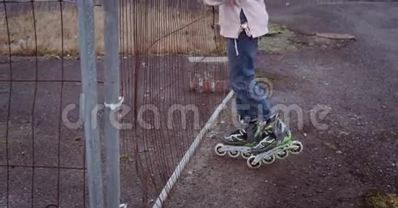 穿着溜冰鞋的年轻女孩用手拿着生锈的栅栏透过它们看女孩穿着粉色背心视频的预览图