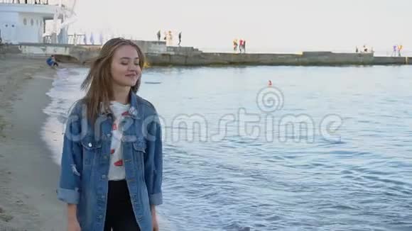 慢动作肖像可爱的年轻女子她在相机中姿势和微笑站在凉爽的夏日海滩上视频的预览图