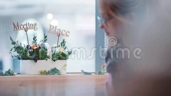 漂亮的金发女孩戴着眼镜坐在舒适的咖啡馆A打电话微笑着点头协议视频的预览图