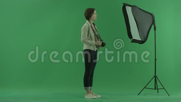 一位年轻女子在绿色屏幕的右手边拍照并纠正了模特的站立姿势视频的预览图