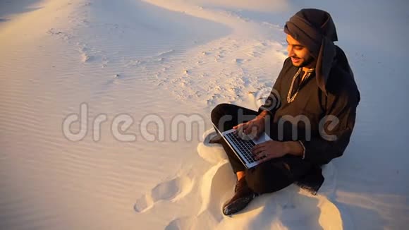 年轻的穆斯林男学生的肖像他们在电脑键盘上打印放松坐在沙地沙漠中视频的预览图