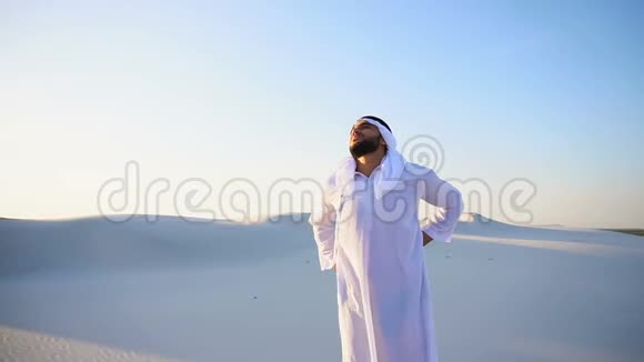 英俊的阿拉伯酋长背部不适站在沙地沙漠中炎热的夏季晚上视频的预览图