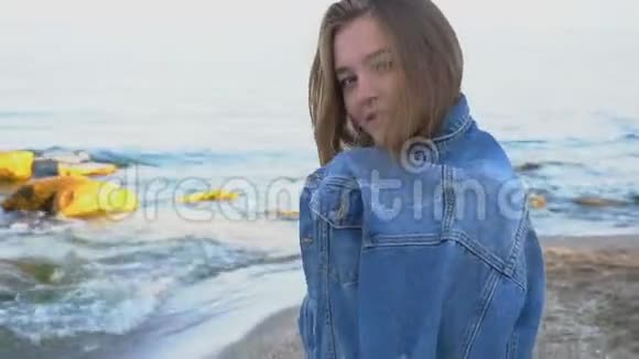 甜美的女人微笑着摆姿势看着地平线在凉爽的夏日站在令人不安的蓝海之滨视频的预览图