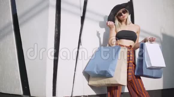 时尚的年轻女性戴着太阳镜帽子和裤子穿着时尚在露天购物中心购物视频的预览图