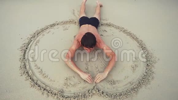 年轻开朗的人仰面躺在沙滩上在海滨潮湿的沙滩上画着一个心的象征慢动作视频的预览图