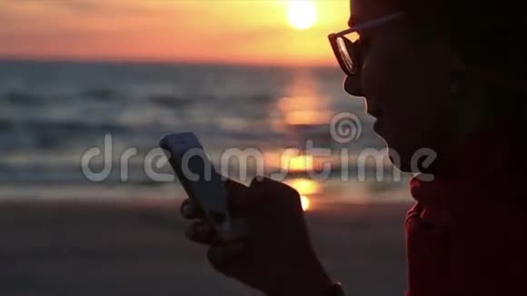 在日落海景女性微笑着用智能手机享受乐趣视频的预览图