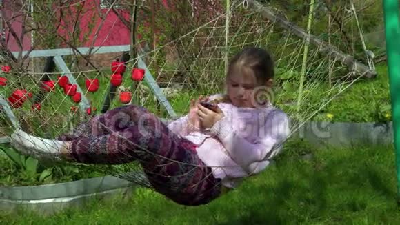 4K女郎在吊床上的肖像演奏儿童脸在大自然中使用智能手机视频的预览图