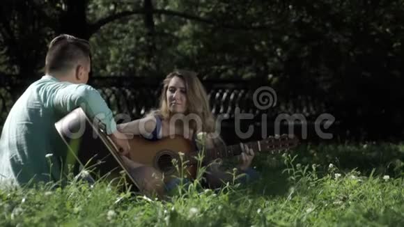 一对相爱的夫妇拿着吉他坐在草地上的公园里视频的预览图