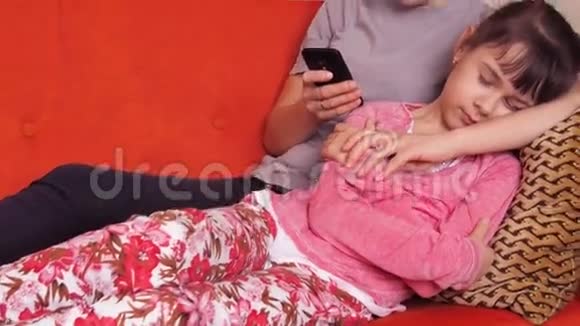 母女俩坐在沙发上用手机妈妈看手机女儿睡觉视频的预览图