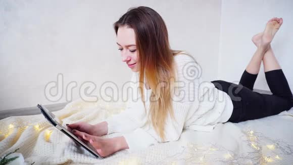 优雅的女孩选择礼物给家庭使用平板电脑躺在地板上的格子在明亮的房间旁边的花环和花环视频的预览图