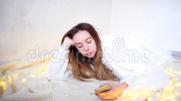 令人沮丧的女人在手机屏幕上读到令人不快的消息躺在明亮的房间里被毯子覆盖的地板上视频的预览图