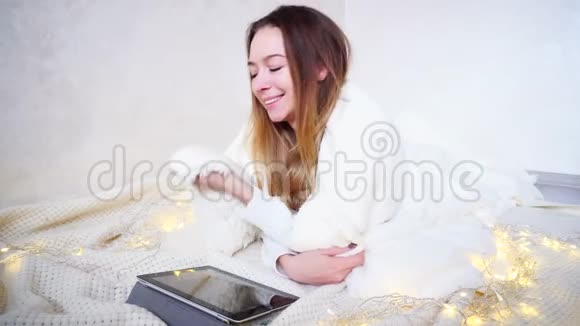 美丽的年轻女子享受温暖和舒适微笑着看着摄像机躺在地板上铺着明亮的毯子视频的预览图