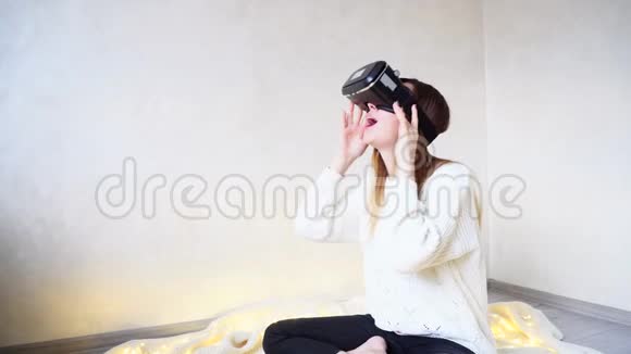 美丽而开朗的女人沉浸在虚拟现实中戴着特殊的现代眼镜坐在明亮的房间里和视频的预览图