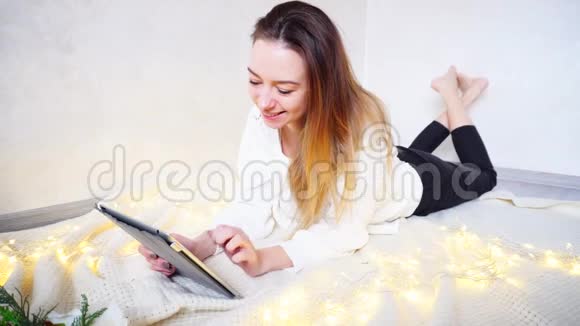 漂亮的年轻女人在网上搜索小玩意寻找聚会的想法躺在旁边明亮的房间里的格子地上视频的预览图