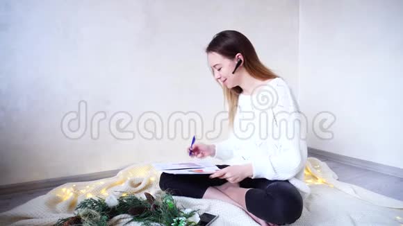 成功的女摄影师在蓝牙耳机上安排会议在家工作坐在格子布上的地板上视频的预览图