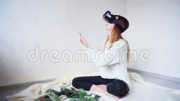 迷人的女孩用虚拟现实眼镜看光圈坐在明亮的房间里里面有花环视频的预览图