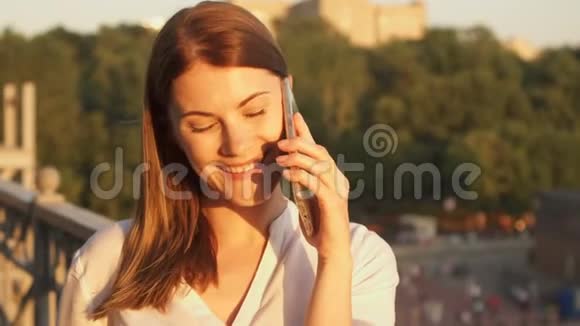 快乐的年轻女人在户外放松漂亮的女孩在她的智能手机上说话夏日阳光灿烂视频的预览图